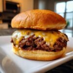 Close-up of a delicious smash burger recipe on a white plate, featuring a golden bun and melted cheese over a savory beef patty.