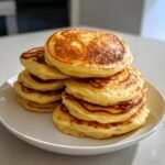 A tall stack of golden-brown sourdough discard pancakes on a white plate, showcasing their fluffy texture.