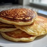 A stack of fluffy sourdough discard pancakes on a white plate, golden brown and perfectly cooked.