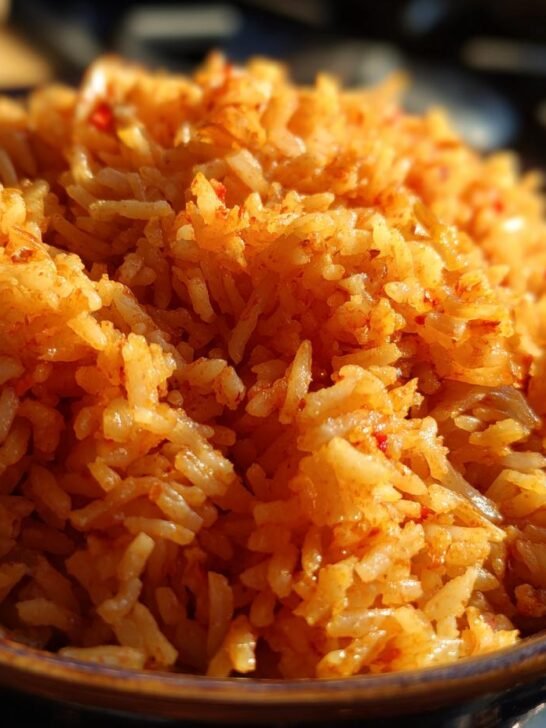 Close-up of a bowl filled with fluffy, orange-hued Spanish rice, seasoned with red spices.