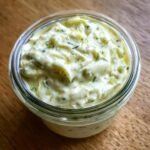 Close-up of creamy homemade tartar sauce recipe in a glass jar, with visible dill and capers.