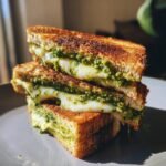 Close-up of a stacked Ultimate Pesto Grilled Cheese sandwich, with melted cheese oozing out and vibrant green pesto visible.