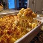 A fork lifting a cheesy portion of Ultimate Southern Baked Mac And Cheese Delight from a casserole dish.