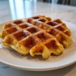 Close-up of two Apple Spice Cornmeal Waffles dusted with cinnamon sugar on a white plate.