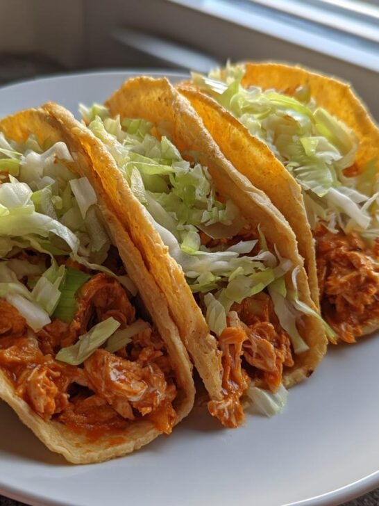 Three crispy tacos filled with shredded orange buffalo chicken and topped with shredded lettuce, representing Baked Buffalo Chicken Tacos Dairy Free.