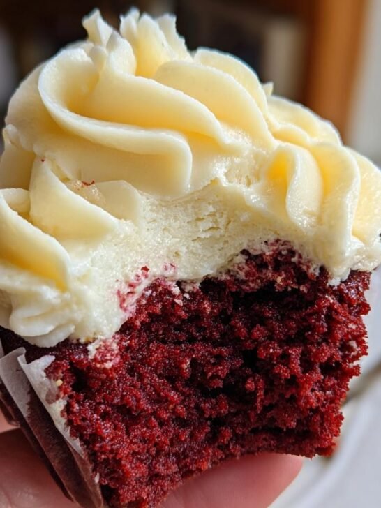 Close-up of a bitten Vegan Red Velvet Cupcakes Bourbon Vanilla Buttercream, showing rich red cake and creamy frosting.