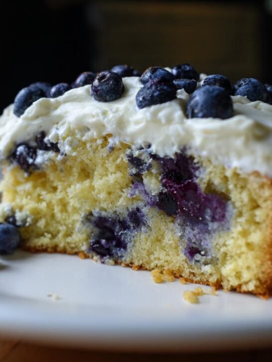 A slice of Blueberry Oatmeal Cake topped with creamy cream cheese frosting and fresh blueberries.