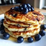 A tall stack of golden-brown Blueberry Whole Wheat Pancakes, topped with fresh blueberries.