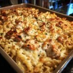 Close-up of a golden-brown baked pasta dish with tender chicken pieces and melted cheese, sprinkled with parsley.