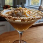 A delicious Caramel Apple Pie Martini topped with whipped cream and caramel drizzle, rimmed with crushed cookies.