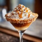 A delicious Caramel Apple Pie Martini topped with whipped cream, caramel drizzle, and cookie crumbs, served over ice.