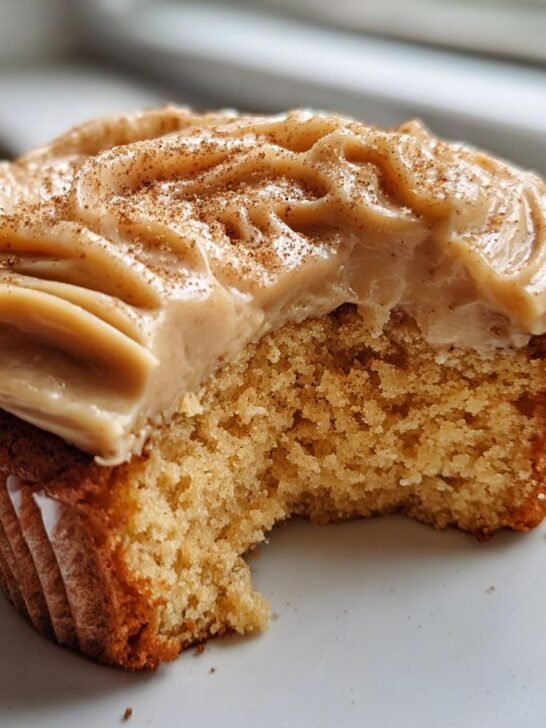 Close-up of a Caramel Eggnog Cupcake with rich frosting and a bite removed, showing the moist crumb.