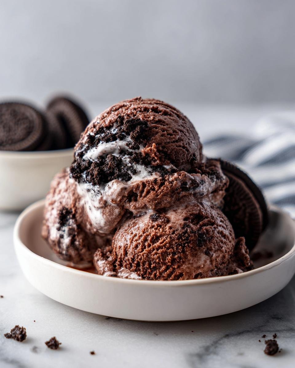 Three scoops of melting Chocolate Oreo Ice Cream No Churn studded with cookie pieces in a white bowl.