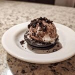 A scoop of Chocolate Oreo Ice Cream No Churn resting on two Oreo cookies, topped with cookie crumbles.