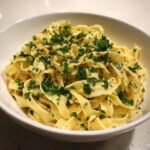A bowl of fettuccine pasta coated in a creamy garlic sauce and topped with fresh parsley.