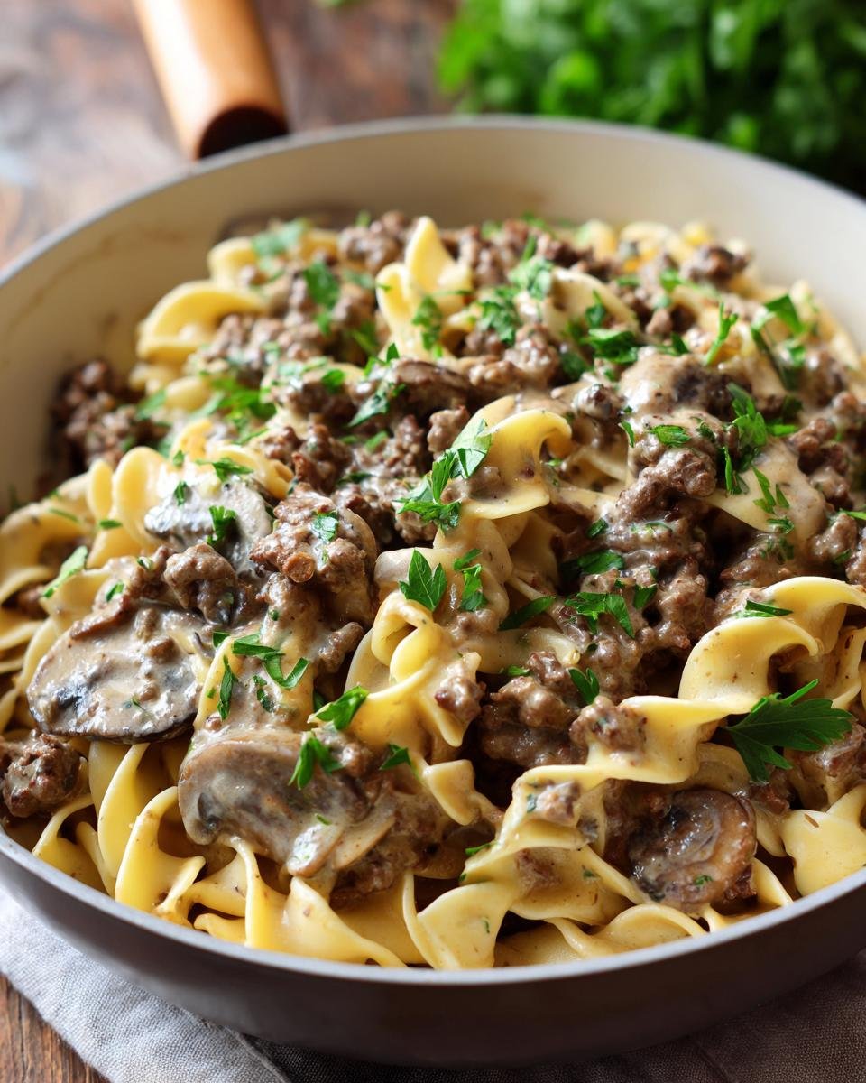 Close-up of a bowl filled with creamy ground beef stroganoff and egg noodles, garnished with fresh parsley.