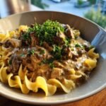 A close-up of a bowl of Creamy Ground Beef Stroganoff served over wide egg noodles, garnished with fresh parsley.