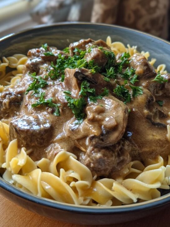 A close-up of a bowl of Creamy Ground Beef Stroganoff Recipe served over egg noodles and garnished with fresh parsley.