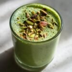 A refreshing glass of creamy pistachio milk topped with chopped pistachios and a sprinkle of spice.