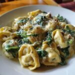 A close-up of Irresistibly Creamy Tortellini With Spinach, topped with grated Parmesan cheese and herbs.