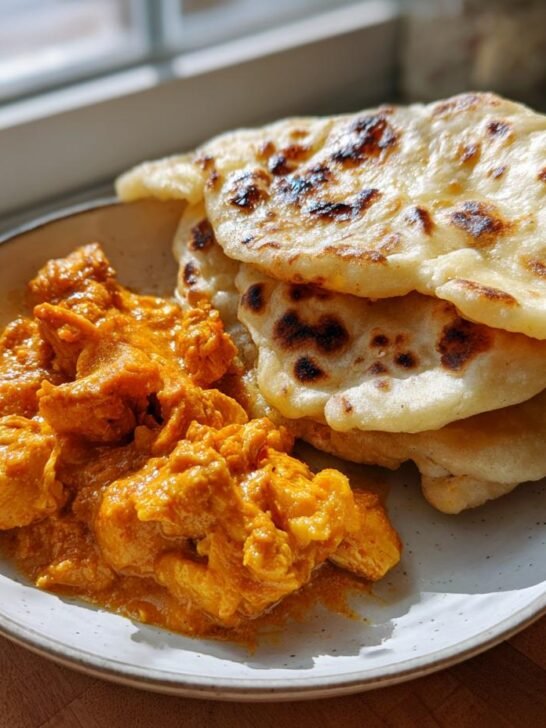A plate featuring vibrant orange Curry Chicken next to a stack of freshly cooked, slightly charred roti bread.