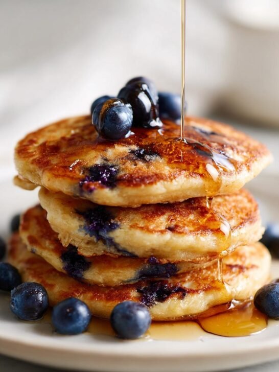 A stack of fluffy Dairy Free Almond Blueberry Pancakes topped with fresh blueberries and drizzled with syrup.