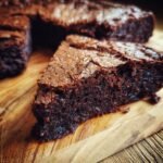 A close-up of a rich, dark chocolate slice of Decadent Brown Butter Brownies on a wooden board.