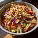 A bowl of Delicious Asian Chicken Crunch Salad with shredded chicken, cabbage, carrots, peanuts, and sesame seeds.