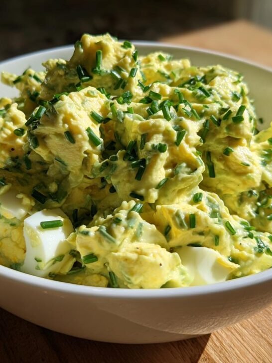 A bowl of delicious keto avocado egg salad topped with fresh chives, showing chunks of hard-boiled egg.