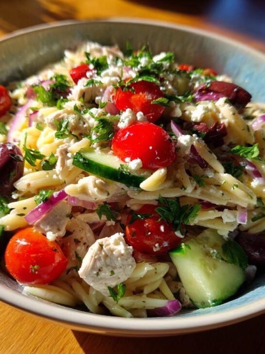 A close-up of a bowl filled with Delightful Mediterranean Chicken Pasta Salad, featuring orzo pasta, chicken, cherry tomatoes, cucumber, olives, and feta cheese.