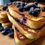A stack of golden brown Easy Dairy Free Blueberry French Toast topped with fresh blueberries and powdered sugar.