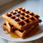 A stack of two golden brown Easy Vegan Gluten Free Gingerbread Waffles drizzled with syrup on a white plate.