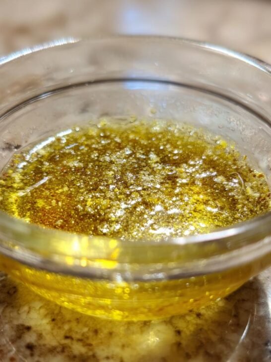 Close-up of freshly mixed Everyday Lemon Vinaigrette Dressing, showing separated oil and spices in a small glass bowl.