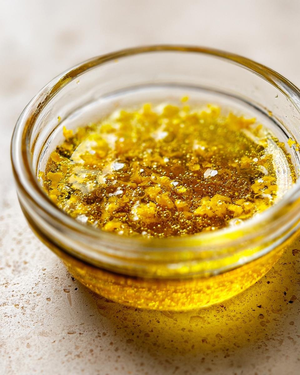 Close-up of bright yellow lemon zest and oil mixture for Everyday Lemon Vinaigrette Dressing in a small glass bowl.