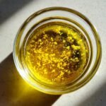Overhead view of bright yellow lemon zest floating in oil for Everyday Lemon Vinaigrette Dressing in a small glass jar.