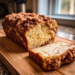 A slice of Fluffy Cinnamon Crunch Bread on a wooden cutting board, showcasing its crumbly cinnamon topping and swirled interior.