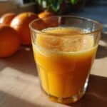 A close-up of a glass filled with freshly squeezed orange juice, with whole oranges in the background.