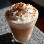 A cold Gingerbread Eggnog Mocktail in a glass, topped with whipped cream and a sprinkle of cinnamon.