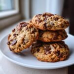 A stack of four freshly baked Grandmas Chocolate Chip Pecan Cookies piled on a white plate.