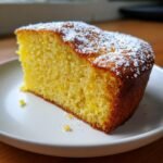 A slice of moist Grapefruit Olive Oil Cake dusted with powdered sugar on a white plate.