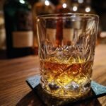 A glass of Hakushu 12 Year Whisky on a wooden table with bottles in the background.