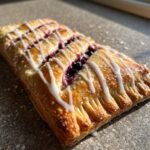 Close-up of a golden-brown homemade blueberry vegan pop tart drizzled with white icing.