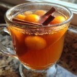Close-up of a glass mug filled with warm Homemade Slow Cooker Apple Cider, garnished with whole spices and orange slices.