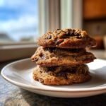 A stack of three golden brown Hubbys Maple Chocolate Chip Cookies piled high on a white plate.