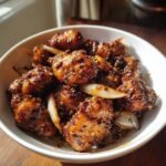 A bowl of Irresistible Black Pepper Chicken with onions, coated in a glossy, dark sauce with visible peppercorns.