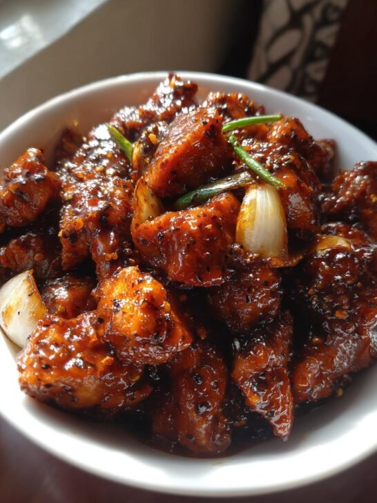 A close-up shot of Irresistible Black Pepper Chicken, glistening with a dark sauce and sprinkled with black pepper.