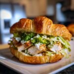 A close-up of an Irresistible Chicken Caesar Croissant Sandwich filled with tender chicken, crisp lettuce, and creamy Caesar dressing.