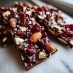 Close-up of Irresistible Chocolate Bark, topped with whole almonds, chopped nuts, and dried cranberries.