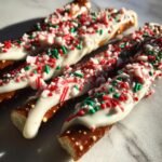 Close-up of Irresistible Christmas Pretzels dipped in white chocolate and topped with crushed candy canes and festive sprinkles.