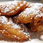 Close-up of Irresistible Funnel Cake Bites dusted generously with powdered sugar.